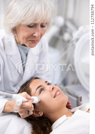 Elderly female beautician doing procedure of microneedling, mesotherapy for young woman in beauty salon indoors 112788794