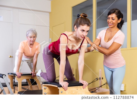 Young woman performs an exercise on a combined chair with instructor 112788874