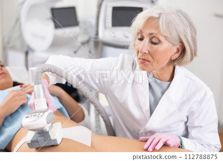 Old woman specialist doing LPG massage of hips of young woman Old woman specialist doing LPG massage of hips of young woman 112788875