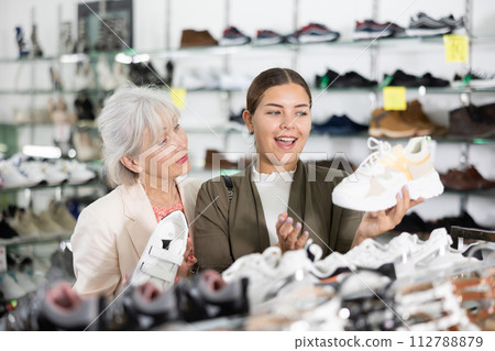 Two positive women of different ages choose new sneakers together in fashion store Two positive women of different ages choose new sneakers together in fashion store 112788879