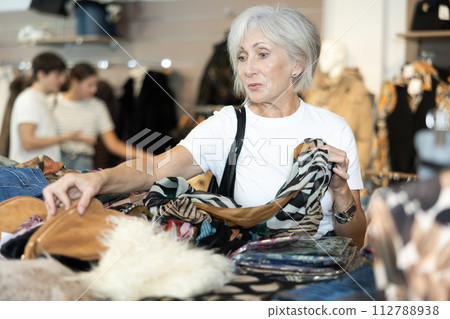 Old woman choosing second hand clothes in large clothing shop Old woman choosing second hand clothes in large clothing shop 112788938