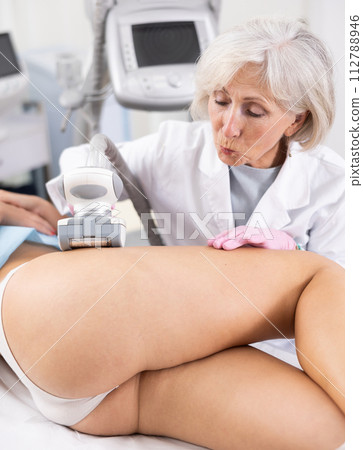 Old woman specialist doing LPG massage of hips of young woman 112788946