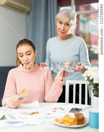 Young woman holding out banknotes to aged mother at home table 112788949