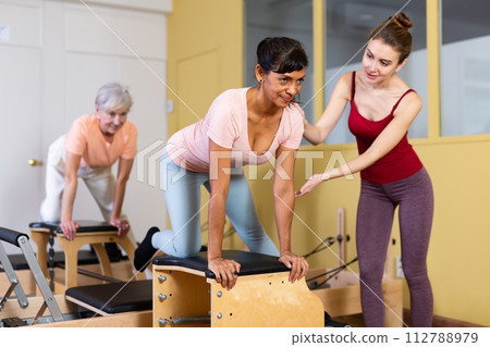 Hispanic woman practicing pilates on wunda chair with young trainer 112788979