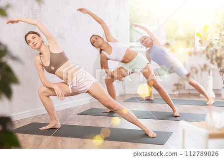 Mom, grandma and teenage daughter do variation lateral elongated angle pose Utthita Parshvakonasana. 112789026