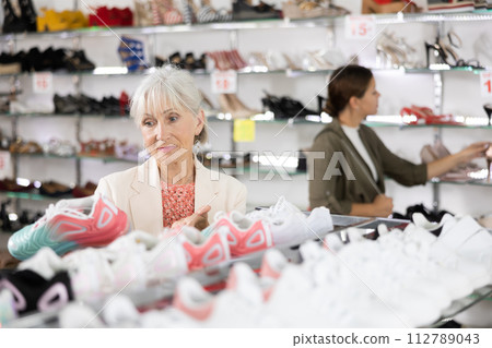 Elderly woman chooses modern sports shoes in shoe store Elderly woman chooses modern sports shoes in shoe store 112789043