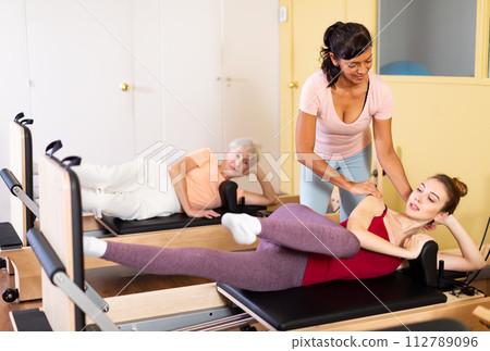 Young woman practicing pilates on reformer with female trainer 112789096