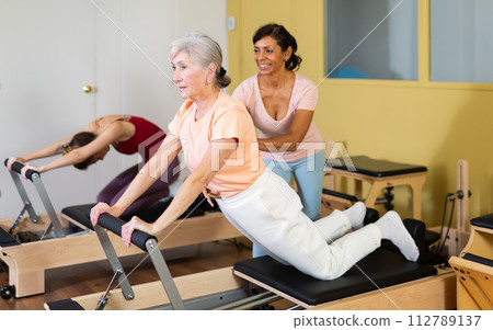 Elderly woman practicing pilates on reformer with Hispanic female trainer 112789137