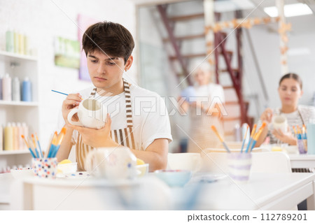 Talented young artisan applying design to ceramic mug in pottery studio Talented young artisan applying design to ceramic mug in pottery studio 112789201
