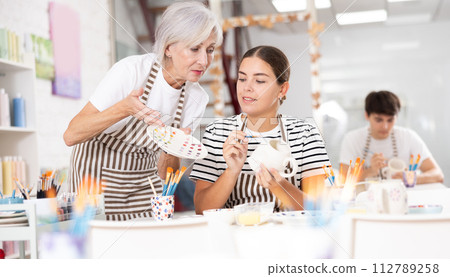 Experienced female ceramicist teaching young girl to paint ceramics in pottery studio 112789258