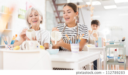 Cheerful young girl working with elderly mother in family pottery studio 112789283