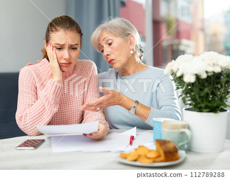 Worried elderly woman and adult daughter looking at papers at home 112789288