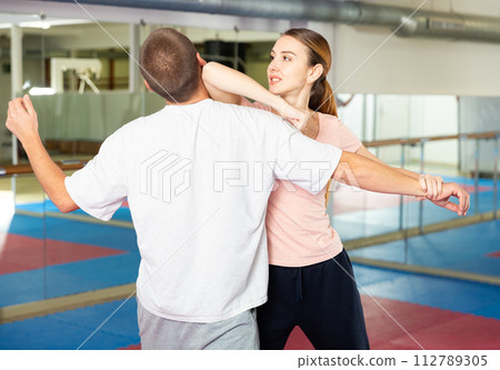 Girl performing elbow strike and wristlock to man in self defence training 112789305