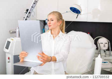 Young woman looking in mirror after cosmetological procedures 112789332
