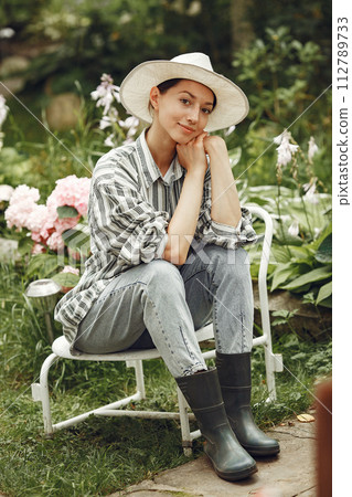 Young woman taking care of plants. Brunette in a hat and gloves. 112789733
