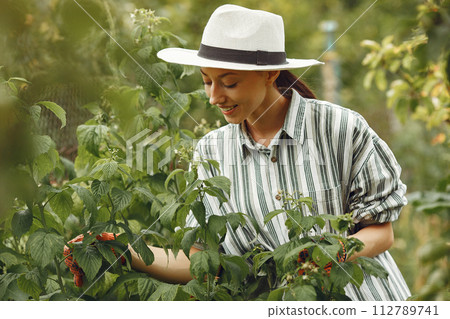 Young woman taking care of plants. Brunette in a hat and gloves. 112789741