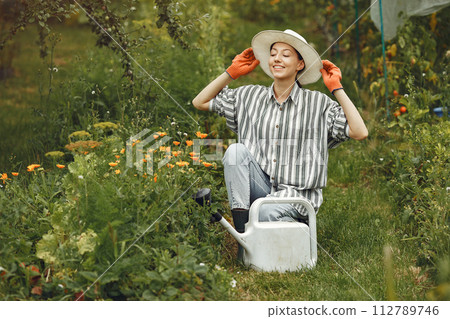 Gardening in summer. Woman watering flowers with a watering can. Girl wearing a hat. Gardening in summer. Woman watering flowers with a watering can. Girl wearing a hat. 112789746