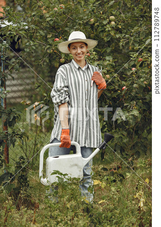 Gardening in summer. Woman watering flowers with a watering can. Girl wearing a hat. Gardening in summer. Woman watering flowers with a watering can. Girl wearing a hat. 112789748