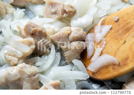 A cooking scene in which chicken thighs and onions are stir-fried in a frying pan. 112790778