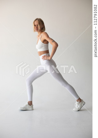 Beautiful blonde girl posing on a white background in white leggings and a white top 112791082