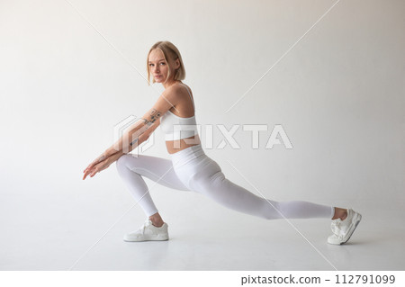 Beautiful blonde girl posing on a white background in white leggings and a white top 112791099