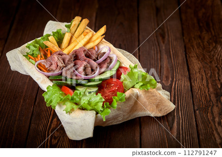 Meat salad with beef and fresh vegetables and lettuce in a plate-baked pita bread. Copy space, wooden background. 112791247