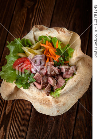 Meat salad with beef and fresh vegetables and lettuce in a plate-baked pita bread. Copy space, wooden background. Meat salad with beef and fresh vegetables and lettuce in a plate-baked pita bread. Copy space, wooden background. 112791249
