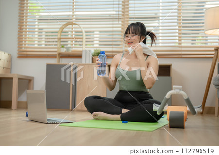 A healthy, fit young Asian woman in sportswear is taking a break after exercise, sipping water. A healthy, fit young Asian woman in sportswear is taking a break after exercise, sipping water. 112796519