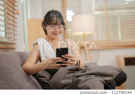 A woman is using her phone and relaxing on the sofa in her living room after finishing her workout. A woman is using her phone and relaxing on the sofa in her living room after finishing her workout. 112796544