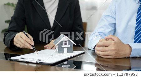 A real estate agent with a House model is talking to clients about buying home insurance. Home insurance concept A real estate agent with a House model is talking to clients about buying home insurance. Home insurance concept 112797958