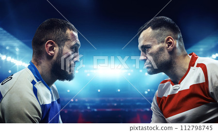 Two American football players standing closely and looking at each other with intense gaze against blurred stadium background. Two American football players standing closely and looking at each other with intense gaze against blurred stadium background. 112798745