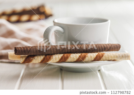 Assorted Chocolate and Vanilla Cream Filled Wafer rolls and coffee cup on white table. Assorted Chocolate and Vanilla Cream Filled Wafer rolls and coffee cup on white table. 112798782