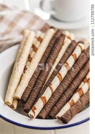 Assorted Chocolate and Vanilla Cream Filled Wafer rolls in bowl on white table. 112798786