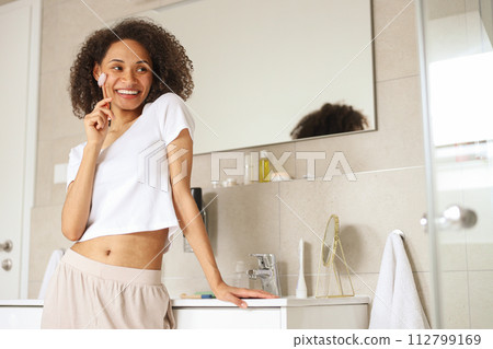 A woman with a smile is brushing her teeth in a bathroom A woman with a smile is brushing her teeth in a bathroom 112799169