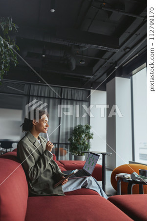 Comfortably sitting on red couch in in nice modern coworking office, using laptop computer Comfortably sitting on red couch in in nice modern coworking office, using laptop computer 112799170