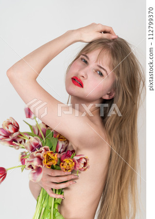 Portrait of woman holding bouquet of spring tulip flowers in hand, covering chest, looking at camera. Woman exudes confidence, femininity. Better Day to Celebrate Beauty on International Women's Day 112799370