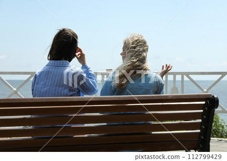 Two girls are talking while sitting on a bench Two girls are talking while sitting on a bench 112799429