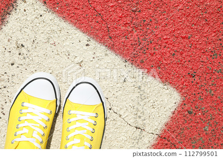 Stylish yellow sneakers on women's legs on the asphalt Stylish yellow sneakers on women's legs on the asphalt 112799501