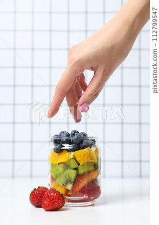 Fruit salad in a glass, transparent jar, on a light background. 112799547