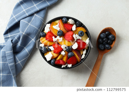 A dark plate with fruit salad on a light table. 112799575