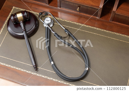 A close-up of a judge's gavel and a black stethoscope on top of a legal book, signifying the intersection of law and medicine. 112800125