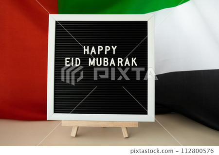 Message text HAPPY EID MUBARAK - happy holidays waving UAE flag on background concept. Greeting card advertisement. Commemoration Day Muslim Ramadan Blessed holy month public holiday 112800576
