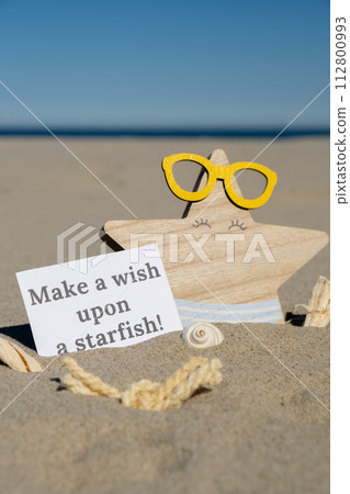 MAKE A WISH UPON A STARFISH text on paper greeting card on background of funny starfish in glasses summer vacation decor. Sandy beach sun coast. Holiday concept postcard. Getting away Travel MAKE A WISH UPON A STARFISH text on paper greeting card on background of funny starfish in glasses summer vacation decor. Sandy beach sun coast. Holiday concept postcard. Getting away Travel 112800993