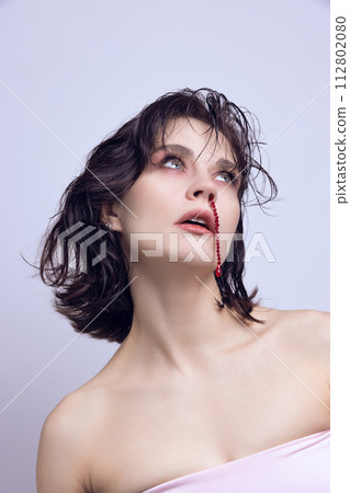 Beautiful, tender young woman with red jewelry imitating nose blood. Glamour impact on self-acceptance. Cosmetic surgery 112802080