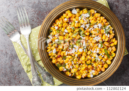 Mexican street corn snack Esquites with added sauce, chili, onion and cheese close-up in a plate on the table. Horizontal top view 112802124