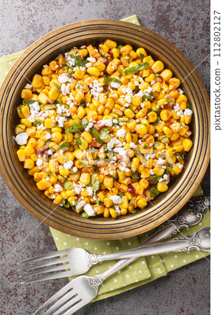 Esquites Mexican Street Corn Salad with jalapeno, cilantro, Cotija cheese, onion and spices close-up on the plate. Vertical top view 112802127