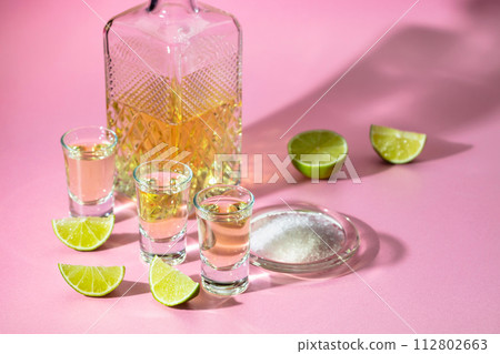 Tequila with salt and lime slices on a pink background. Tequila with salt and lime slices on a pink background. 112802663