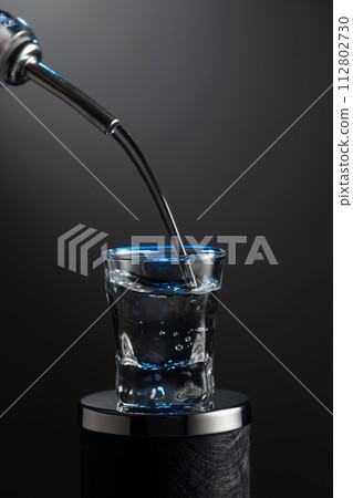 Vodka pouring from the bottle into a glass on a dark background. 112802730