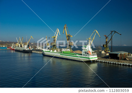 Cargo ship docking at seaport for transshipment. Cranes load containers for international trade. Maritime transport, global business, shipping industry, logistic operations, export in harbor. 112803059