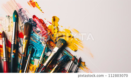 An arrangement of colorful paintbrushes dipped in various hues of paint on a pristine white surface 112803070